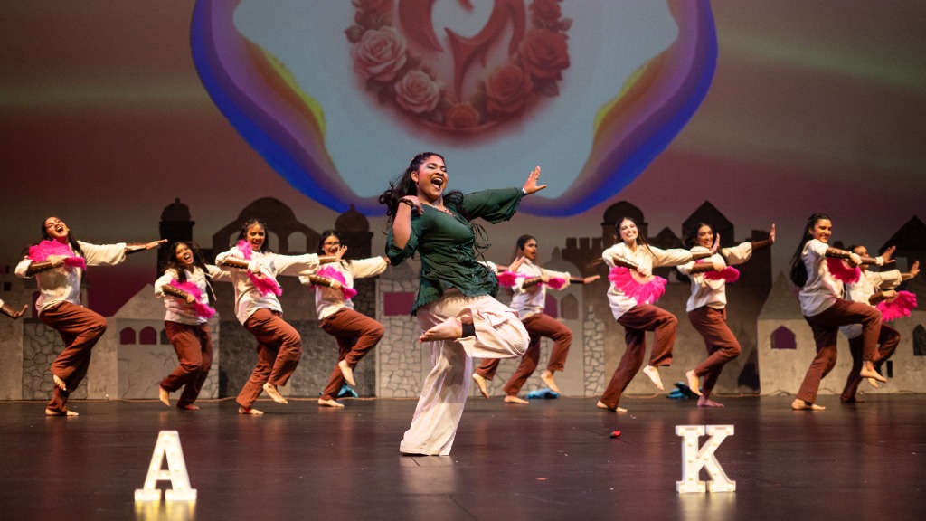 Female dancer in dark green shirt dancing in front with other dancers posing behind